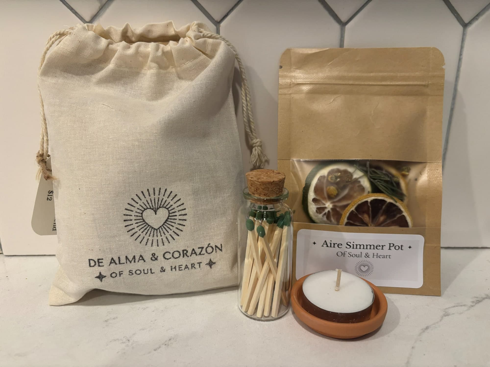 An Aire simmer pot of dried citrus and herbs beside a cotton De Alma y Corazón bag, matches and a tealight in terracotta