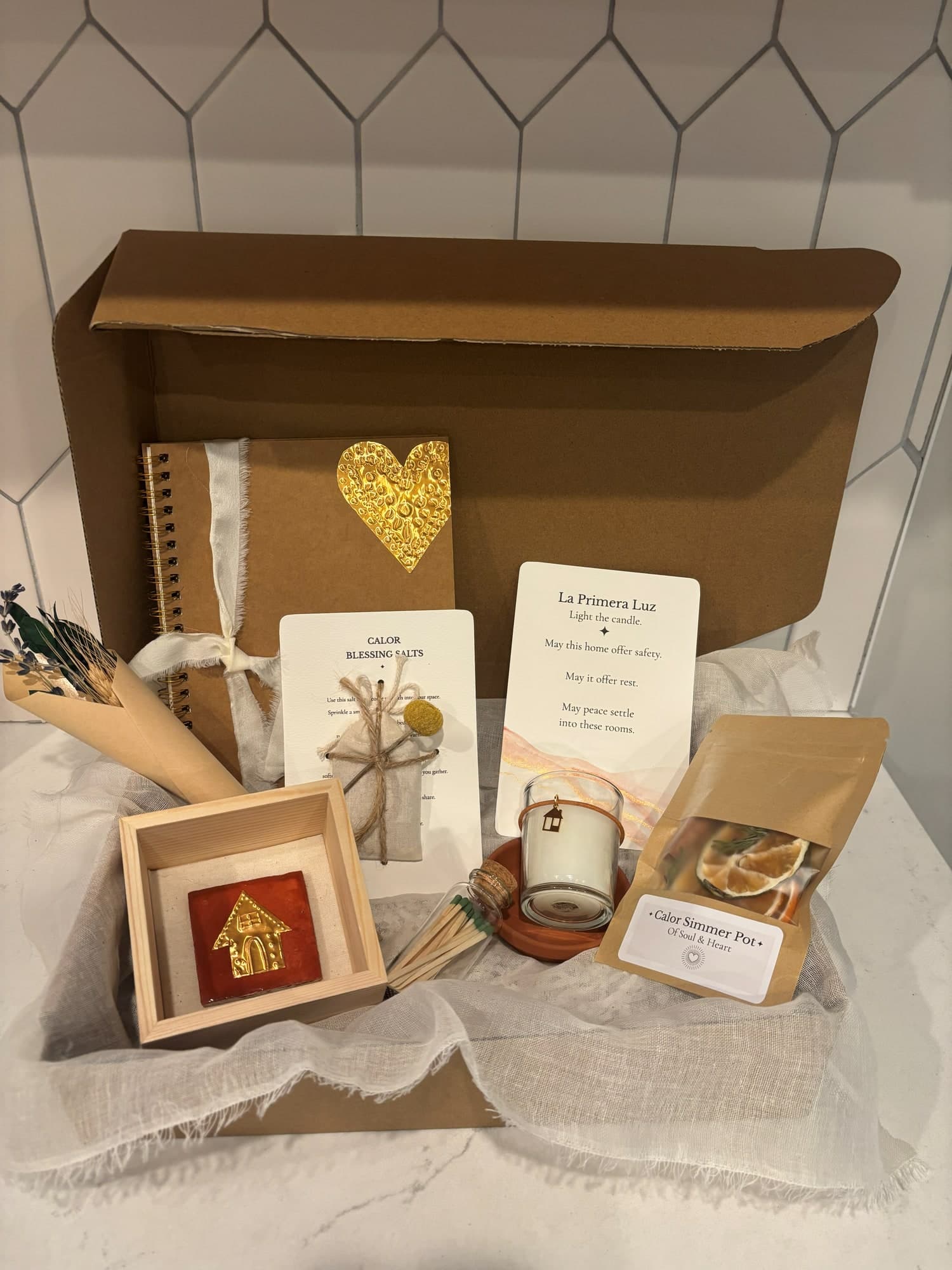 A Casa box packed for a new home, with a gold-heart journal, La Primera Luz card, Calor blessing salts, a framed terracotta house tile and a simmer pot - small-batch housewarming gifting